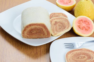 Roll cake (bolo de rolo) next to guavas and a slice of roll cake, blurred in the foreground.