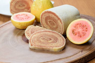 Tahta bir tahtanın üzerindeki guavaların yanında bolo de rolo (rulo kek) dilimleri.