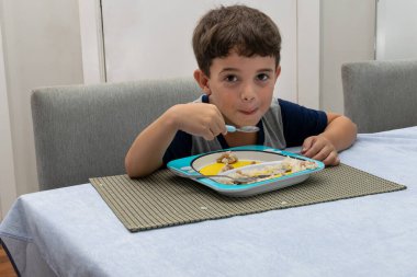 6 year old child having dinner (homemade hamburger, rice and beans) and looking at the camera.