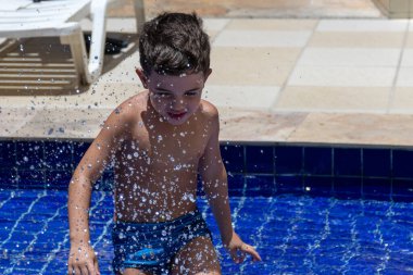 Güneşli bir günde havuz suyunu tekmeleyen 6 yaşında bir çocuk..