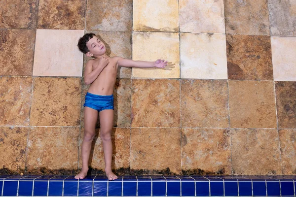 6 yaşında bir çocuk havuzun kenarında komik bir poz veriyor.).