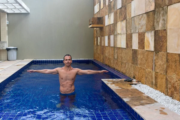 44 year old man, with six pack abs, in the pool and with open arms.