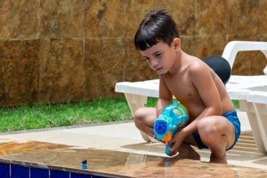 6 yaşında bir çocuk oyuncak bebeğine su tabancasıyla ateş ediyor..