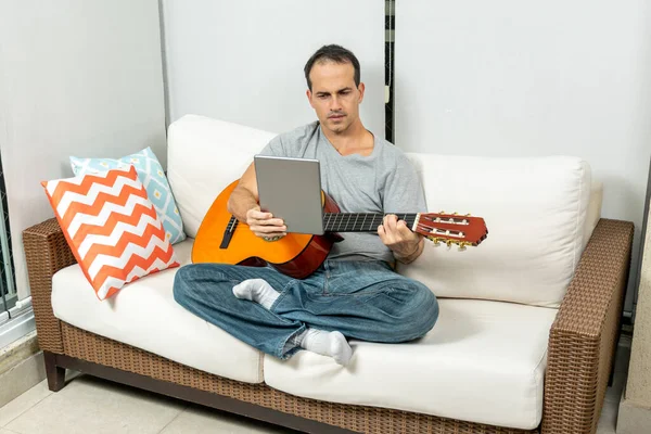 Olgun adam tablette müzik öğreniyor ve gitarda pratik yapıyor..