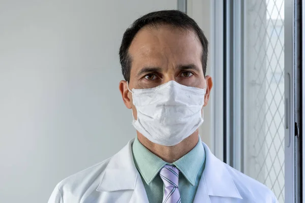 44 year old doctor with mask, white coat and tie.