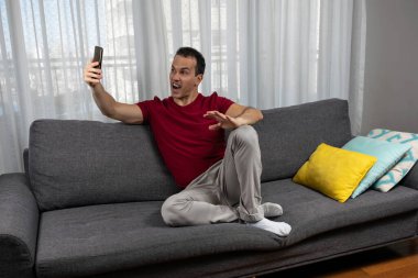 Olgun bir adam (44 yaşında) kanepede oturur ve yüzünü buruştururken fotoğrafını çeker..