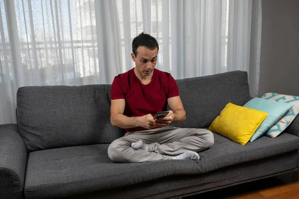 Olgun bir adam (44 yaşında) koltukta bacak bacak üstüne atmış oturuyor ve akıllı telefonunu görünce çok şaşırıyor..