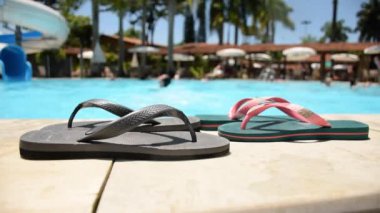 Orta yaşlı bir adam havuz kenarındaki iki çift terliğin üzerinden atlıyor..