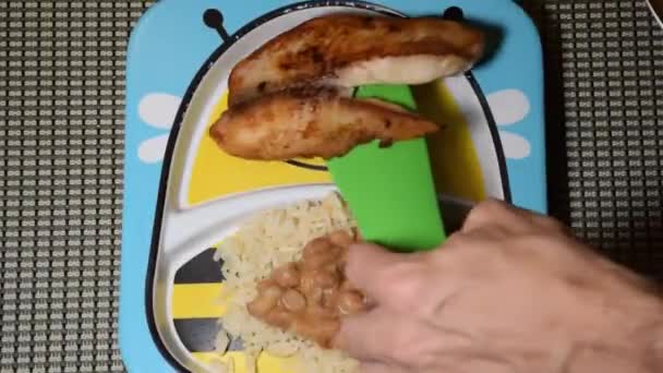 Filé de peixe de tilápia (São Pedro) sendo colocado em um prato infantil com arroz e feijão. — Vídeo de Stock