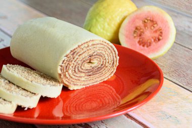 Bolo de rolo (rulo kek) guavaların yanında kırmızı bir tabakta dilimlendi.