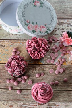 Pembe tereyağlı çikolatalı kekler, yakut çikolata parçacıkları ve yuvarlak bir kutunun yanında..