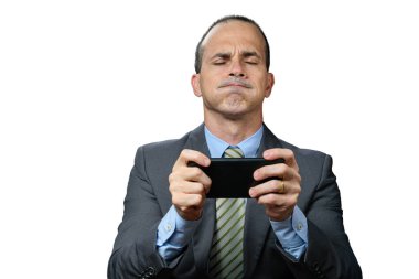 Takım elbiseli ve kravatlı olgun bir adam, akıllı telefonunu yatay olarak tutuyor, burnundan nefes alıyor ve gözleri kapalı..