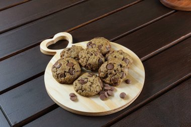 Yuvarlak tahta bir tahtanın üzerinde kalbi olan çeşitli kurabiyeler. Çikolata parçacıklarının yanında..