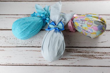 Çikolatalı Paskalya yumurtaları renkli kumaşlar ve beyaz ahşap bir masa üzerinde fiyonklar ile paketlenmiş..