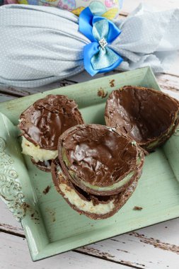 İki parça çikolatalı Paskalya yumurtası beyaz tugaydeiro ve şam fıstıklı brigadeiro. Arka planda, renkli kumaşlarla paketlenmiş Paskalya yumurtaları (dikey fotoğraf)).