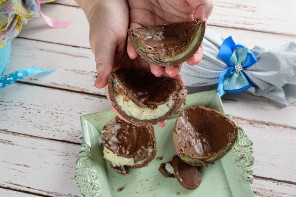 Beyaz tugayla doldurulmuş Paskalya yumurtaları ve şam fıstıklı Brigadeiro taşıyan bir kadın. Arka planda, kurdeleli Paskalya yumurtası.