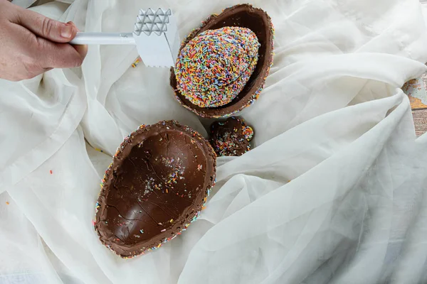 Paskalya yumurtasının (pinata) bir kaç yarısının üzerinde çekiçle bir kadın eli. Renkli çikolata parçacıklarıyla kaplı yumurta..