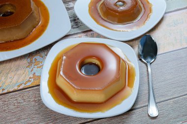 Karamel şurubuyla kaplı konsantre süt pudingi, diğer pudingler ve bir kaşıkla çevrili. Geleneksel Brezilya tatlısıName.