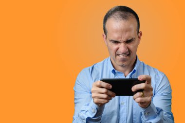 Yetişkin bir adam akıllı telefonuyla oynayıp alt dudağını ısırıyor..