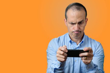 Resmi olarak olgun bir adam akıllı telefonuna bakar ve üst dudağını ısırır. Turuncu arkaplan.