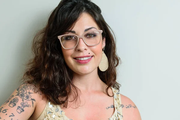 Brazilian woman wearing glasses, tattooed and smiling at the camera.