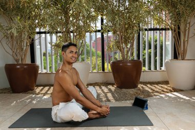 Smiling young Brazilian, taking online yoga class and in the butterfly position.