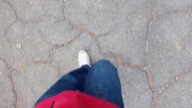 Bakış açısı (POV) videosu, adam beton zeminde kot pantolon ve spor ayakkabılarla yürüyor.