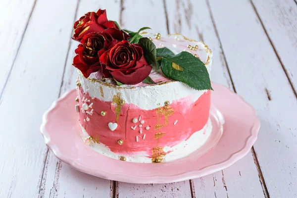 Çikolatalı pasta İsviçre kreması ile kaplı, üstünde üç kırmızı çiçek var. Pembe bir tabakta.