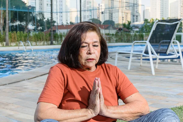 74 years old woman practicing yoga at the edge of the pool.