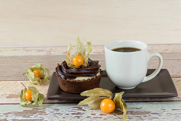 Bir fincan kahvenin yanında, fizsalis ile süslenmiş mascarpone kremalı ve çikolatalı mini turta.).