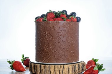 Üzüm ve çilekle süslenmiş çikolata kaplı pasta. Tahta bir kütükte, yüksek anahtarlı bir fotoğrafta..