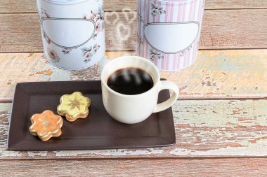 Yenebilir boyalı tereyağlı kurabiyeler bir fincan kahve ve iki teneke kutunun yanında..