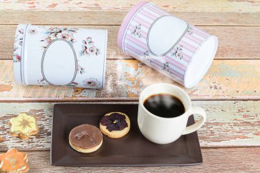 Kurumuş çiçekli tereyağlı bisküvi, diğer bisküvilerin yanında, bir fincan kahve ve teneke kutu..