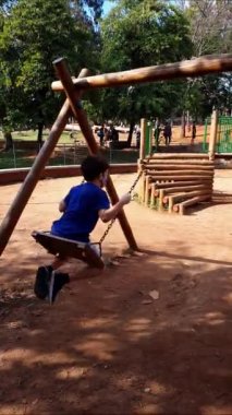 Güneşli bir günde halk meydanında salıncakta sallanan 8 yaşındaki bir çocuk (akıllı telefon videosu)).