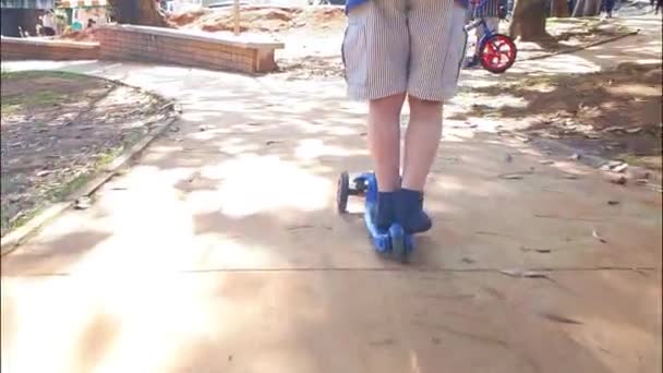 8 letý chlapec kráčí po svahu se svým skútrem na slunečný den na veřejném náměstí. — Stock video
