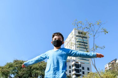 Güneşli bir günde halka açık parkta kollarını açmış 8 yaşında bir çocuk..