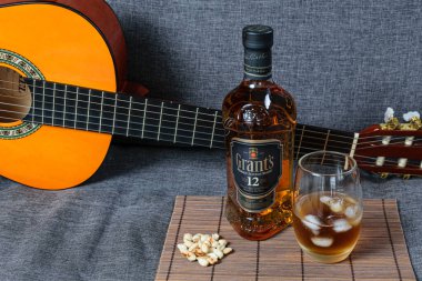 Sao Paulo / Sao Paulo / Brezilya - 1 Ağustos 2020: Arka planda gitar boyunlu, tahta bir paspasın üzerinde, fıstığın yanında 12 yıllık bir şişe viski.