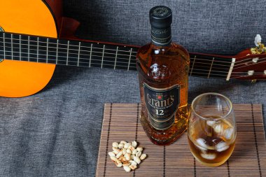 Sao Paulo / Sao Paulo / Brezilya - 01 Ağustos 2020: 12 yıllık viski şişesi, buzlu bardak, kanepenin üzerinde yer fıstığı ve gitar (üstteki manzara)).