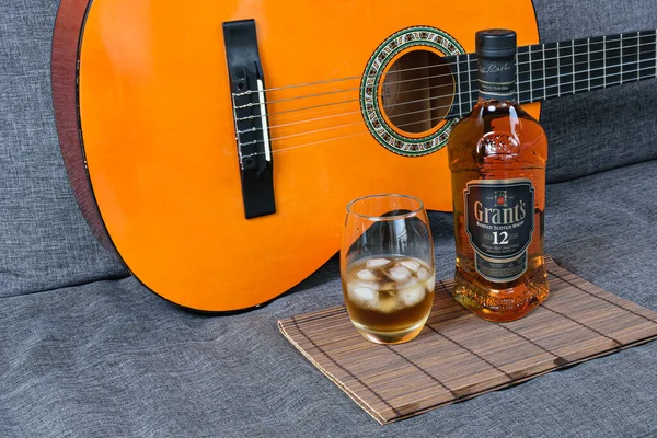 Sao Paulo / Sao Paulo / Brasil - 01 Ağustos 2020 tarihinde: Kahverengi bir halıda buzlu ve bir şişe viskili cam (12 yıllık). Arka planda bir gitar, kanepede..