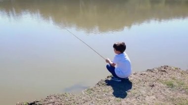 8 yaşındaki Brezilyalı çocuk, pantolonu ve gömleği ile güneşli bir günde gölde balık tutuyor..