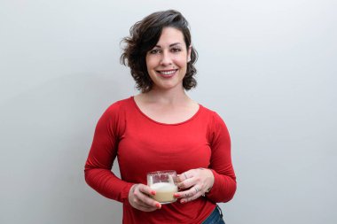 Gülümseyen Brezilyalı kadın kameraya bakıyor ve elinde bir fincan kapuçino tutuyor..