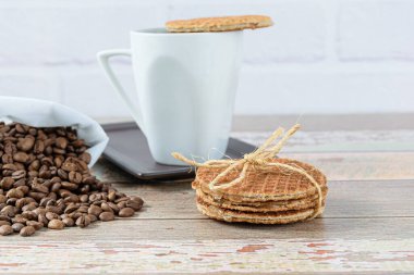 Bir fincan kahvenin yanında sisal yay ile Stroopwafel kurabiyeleri (yan görünüm)).