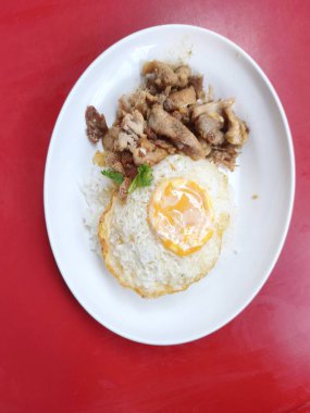 Dikey yemek fotoğrafında çıtır çıtır kızarmış yumurta ile kabarık buğulanmış pirinç üzerine servis edilen yağlı yumurta sarısı ve leziz sotelenmiş domuz dilimleri yer alıyor.