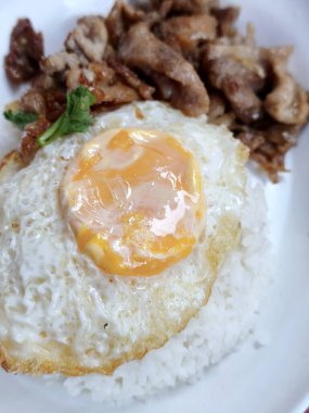 Kıtır kenarlı güneşte kavrulmuş yumurta ve parlak, altın sarısı bir yumurta buharda pişirilmiş beyaz pirinç ve yanında baharatlı domuz dilimleri..