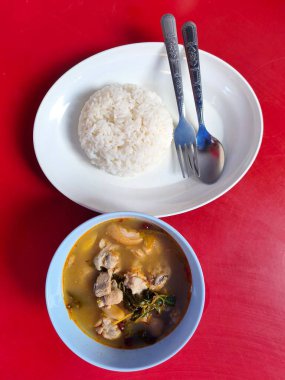 Tayland usulü basit bir yemeğin genel bakış açısında bir kase aromatik tavuk çorbası ve düzgün şekillendirilmiş bir porsiyon beyaz pirinç. Taze tavuk parçaları, bitkiler ve haşlanmış baharatlar var.