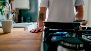 Home kitchen cooking scene with gas stove and frying pan, person standing at kitchen counter, modern interior, everyday lifestyle at home