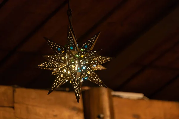 Kırsal bir ahşap evin içinde parıldayan sıcak altın ışıkla parıldayan yıldız şeklinde el yapımı güzel bir lamba. İşçiliği, dekorasyonu ve rahat iç tasarımı temsil eder..