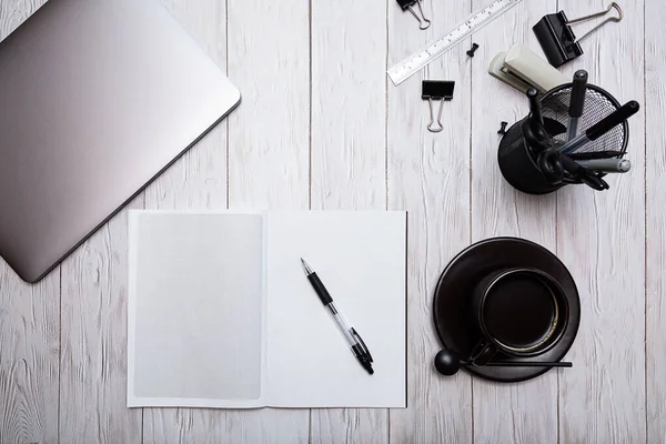 Open squared notebook, laptop, cup of black coffee, stationery on a wooden table top view. Cozy home work place.