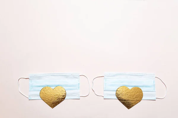 パンデミックの間のバレンタインデーの概念 医療用保護マスクとピンクの背景に金の色のフラットの心の形 — ストック写真