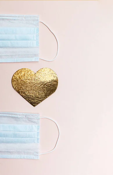 パンデミックの間のバレンタインデーの概念 医療用保護マスクとピンクの背景に金の色のフラットの心の形 — ストック写真